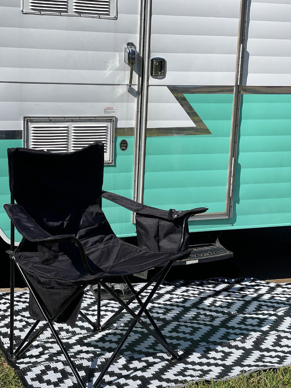 a black and white outdoor camping rug with a black folding camping chair on it