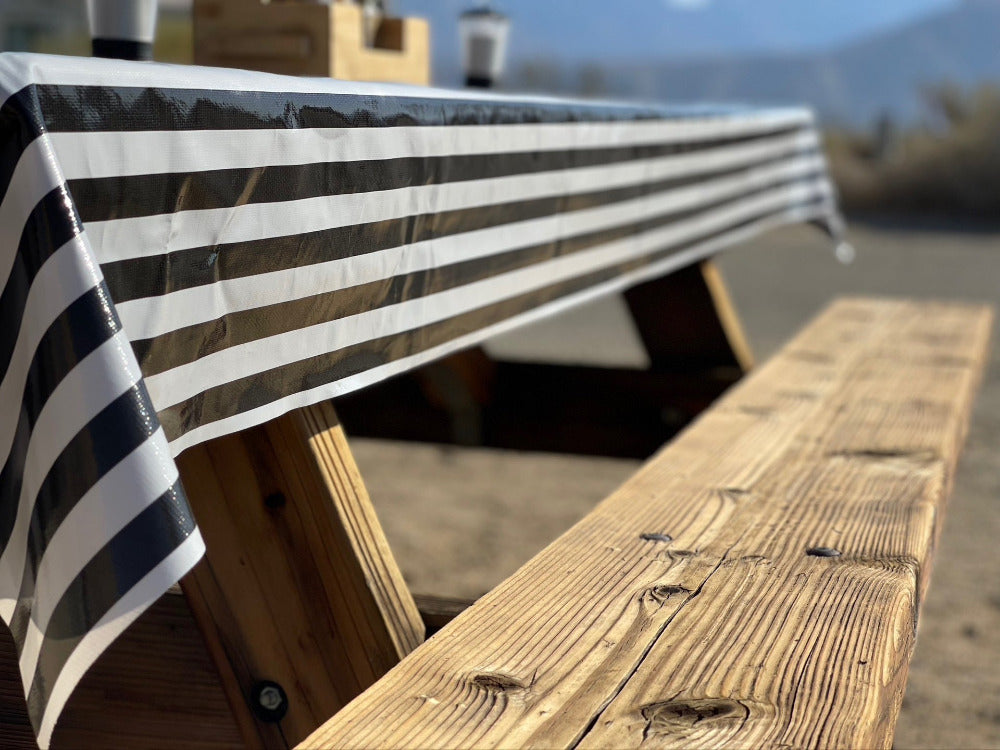 Side view of a black and white striped tablecloth on a wooden campsite picnic table