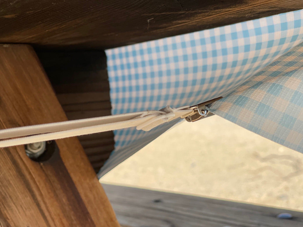 The underside of a wooden picnic table showing a tablecloth strap holding down the tablecloth
