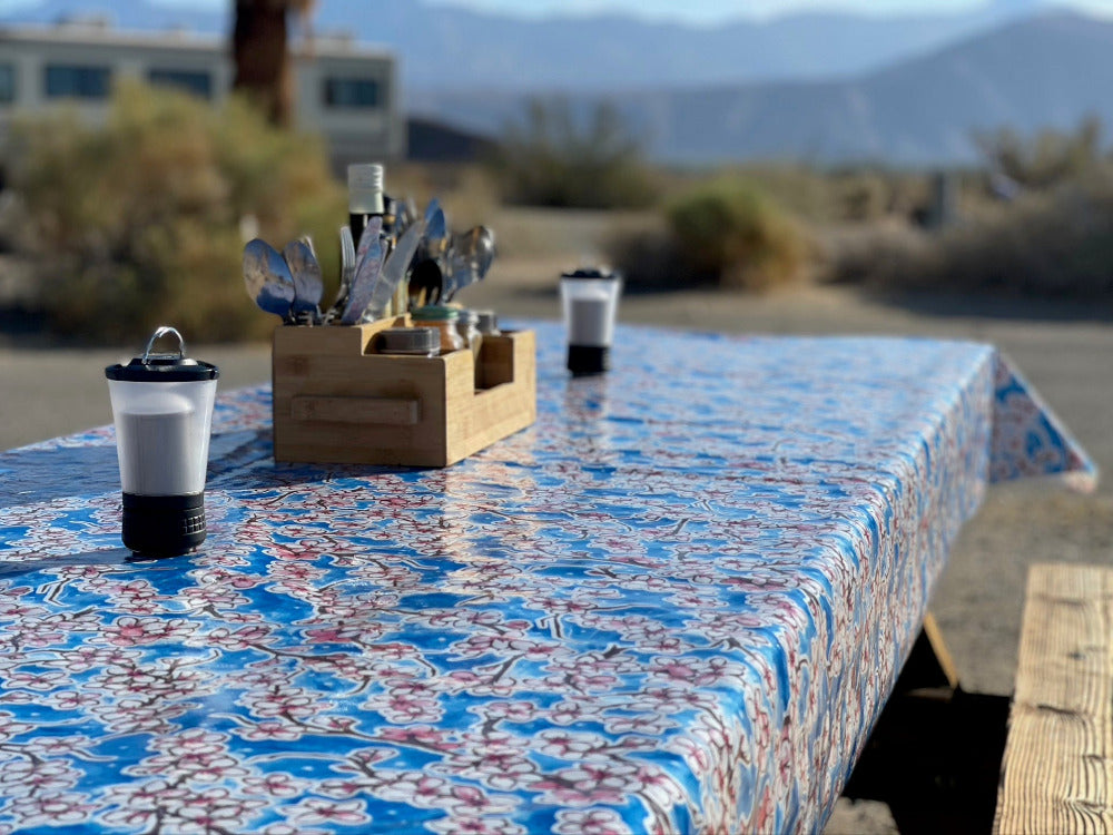 A picnic table with a blue cherry blossom pattern outdoor tablecloth with salt and pepper shakers and a rack with food condiments
